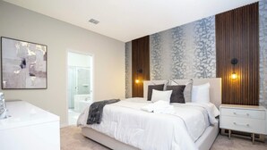 Quarto moderno com uma cama grande, mesas de cabeceira, banheiro com porta de vidro e parede com padrão floral.