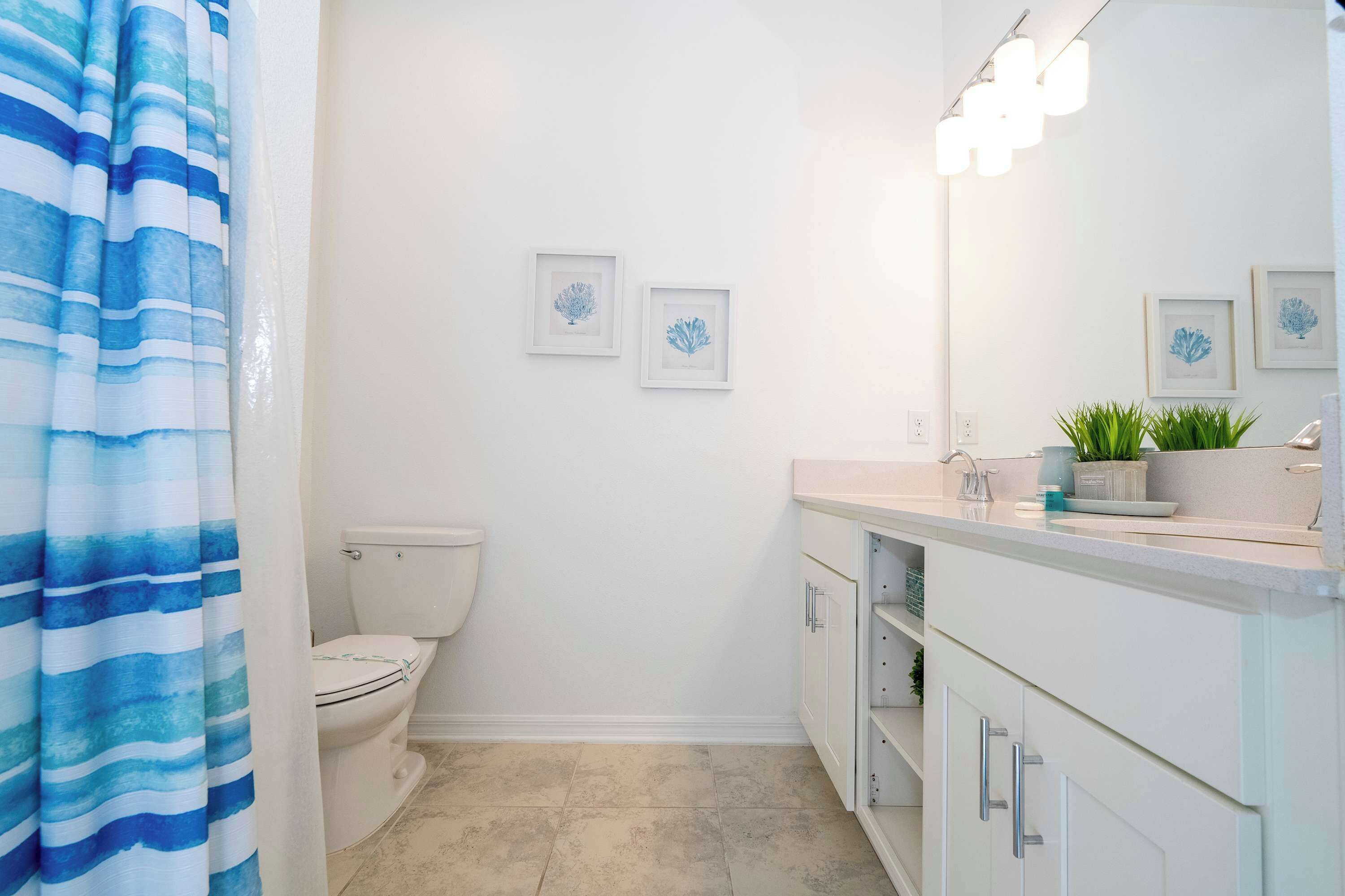 A bathroom with a toilet, a sink with a mirror, and framed artwork on the wall.
