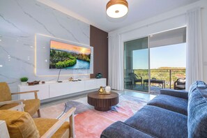 Ein modernes Wohnzimmer mit Flachbildfernseher, einer Couch, einem Couchtisch und Blick ins Freie.