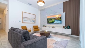 Una sala de estar moderna con un sofá, sillas, un televisor y un detalle decorativo en la pared.