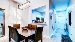 A modern dining area with a rectangular table, four chairs, a hanging light fixture, and a kitchen in the background. - Luxurious Family Townhouse With Private Backyard Retreat (Davenport)