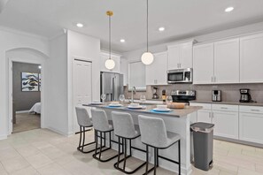 A modern kitchen with white cabinets, a central island with bar stools, a stainless steel refrigerator, and a microwave. - Private Pool & Game Room at Family Villa Near Disney (Kissimmee)