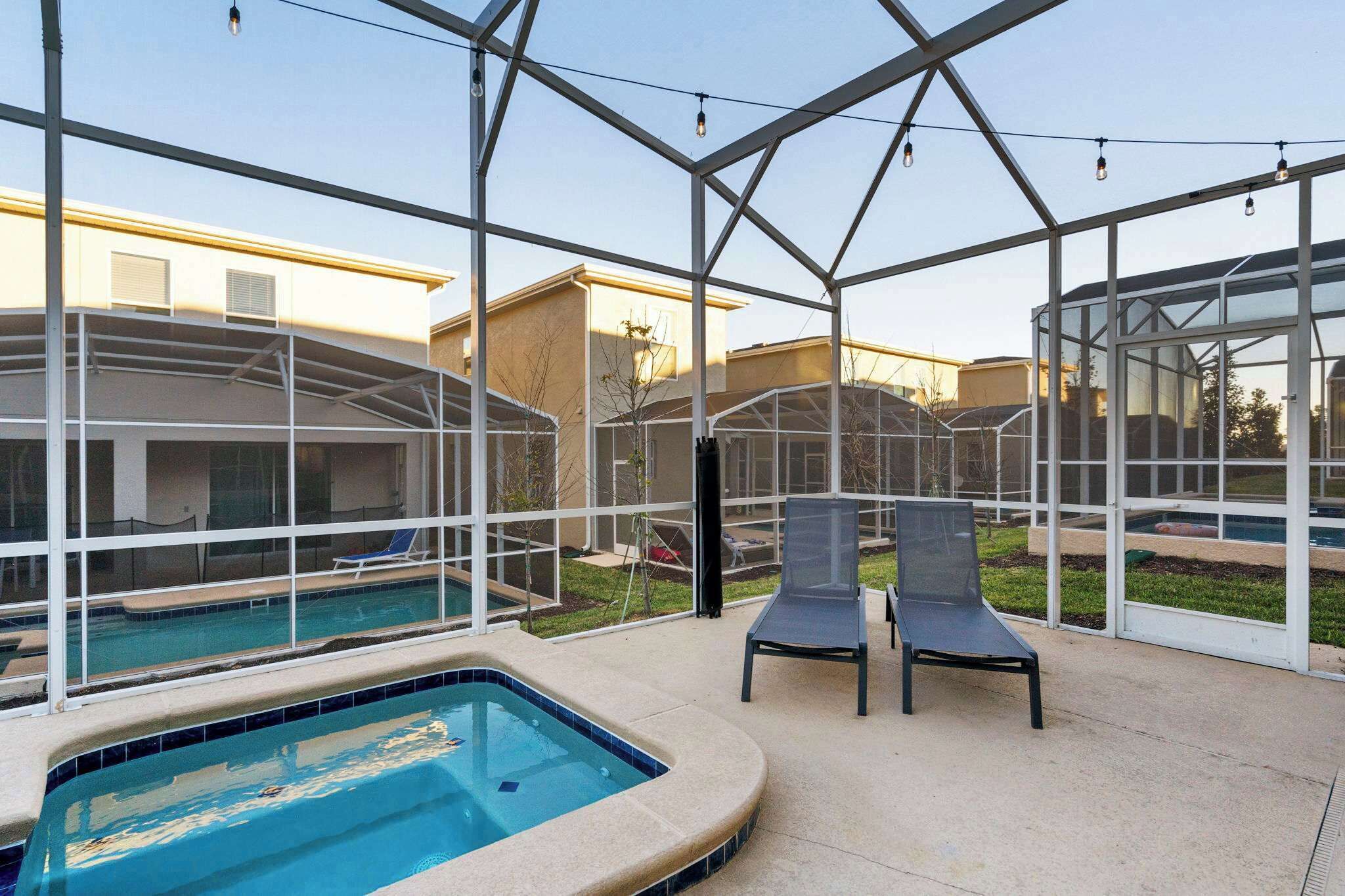 A covered outdoor swimming pool with lounge chairs and a hot tub, surrounded by a glass enclosure.
