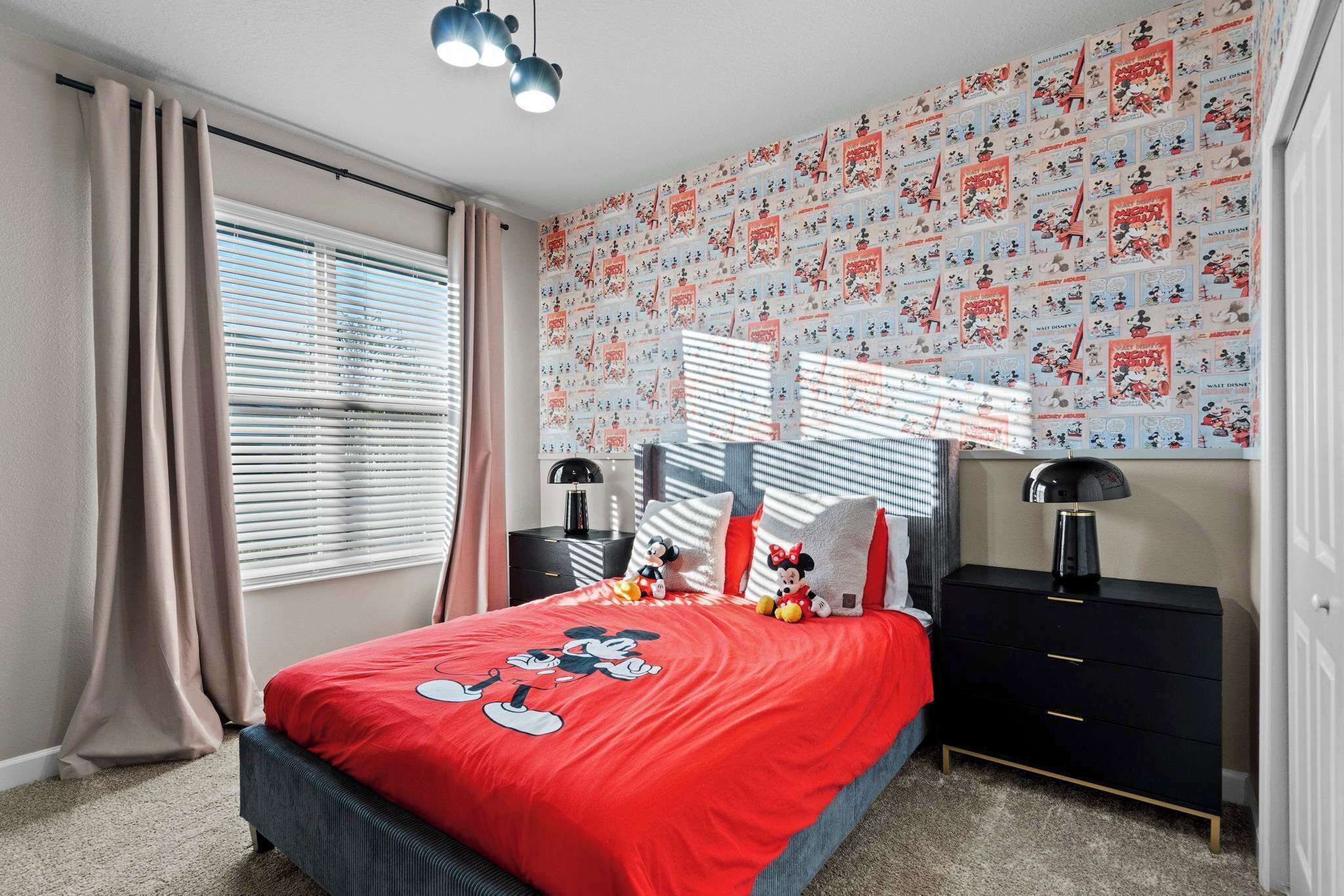 A bedroom with a Mickey Mouse themed bedspread, a black nightstand, and a Mickey Mouse plush toy.