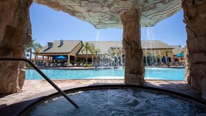 Un bain à remous avec vue sur une piscine et un bâtiment doté d’un toit en tuiles.
