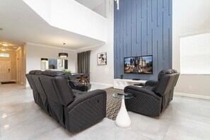 Ein modernes Wohnzimmer mit einem Ecksofa, einem Glastisch und einem Flachbildfernseher, der an einer blauen Akzentwand angebracht ist.
