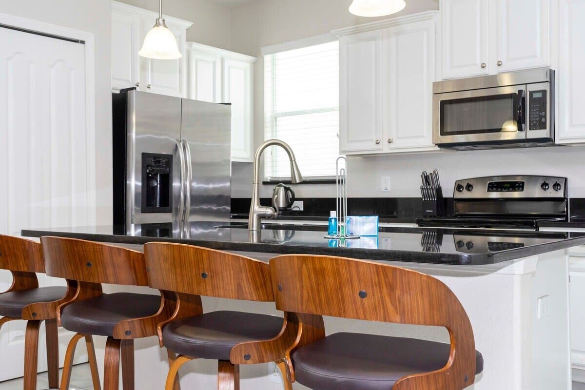 A modern kitchen with white cabinets, stainless steel appliances, and wooden bar stools.
