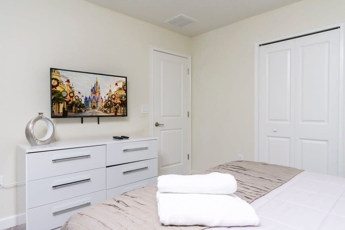 Una camera da letto con un letto, una cassettiera, un quadro raffigurante un castello e due porte bianche.