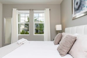 Ein Hotelzimmer mit einem großen Bett, weißen Vorhängen, Blick auf Grün und einem Gemälde an der Wand.