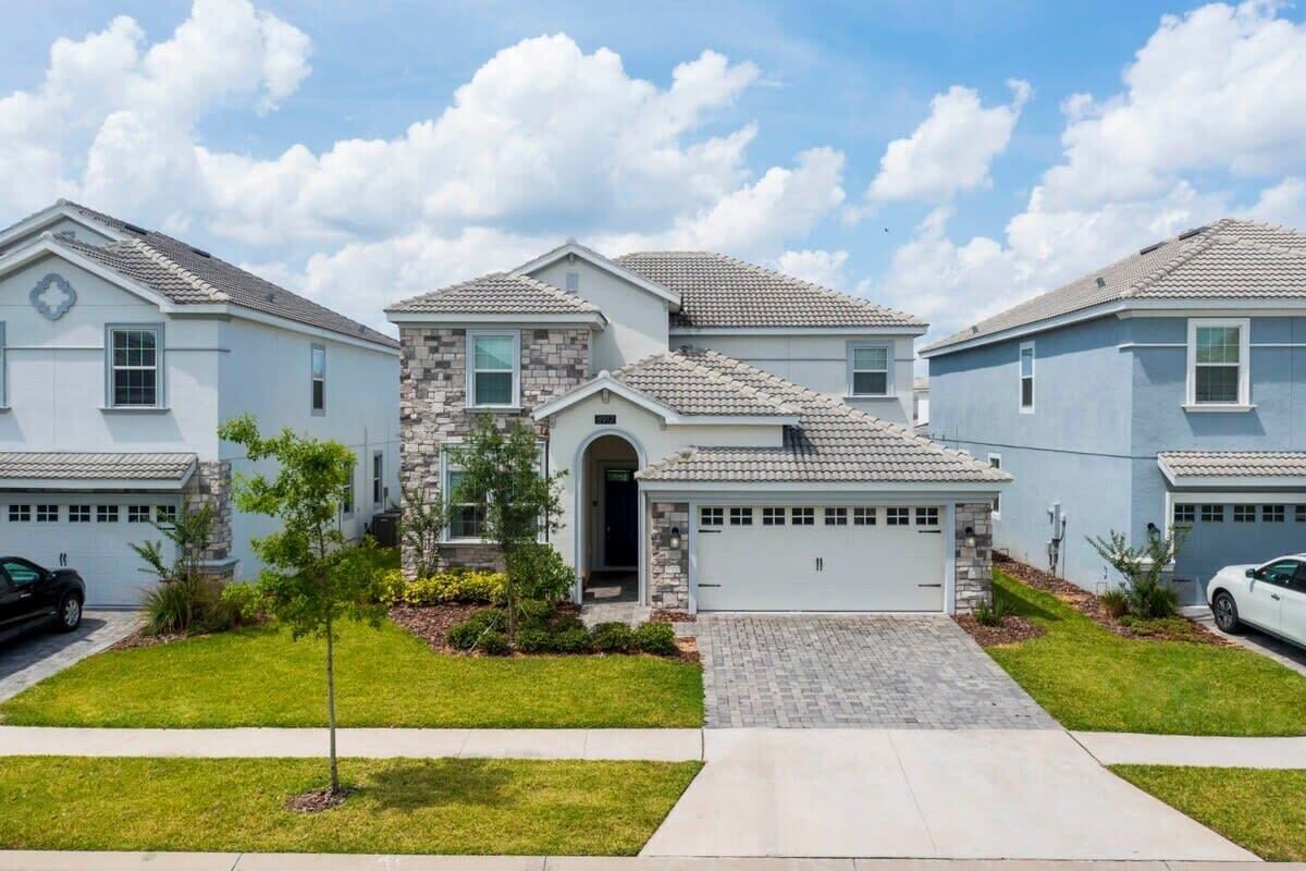 A residential area with houses featuring stone and stucco exteriors, a central driveway, and a clear sky.