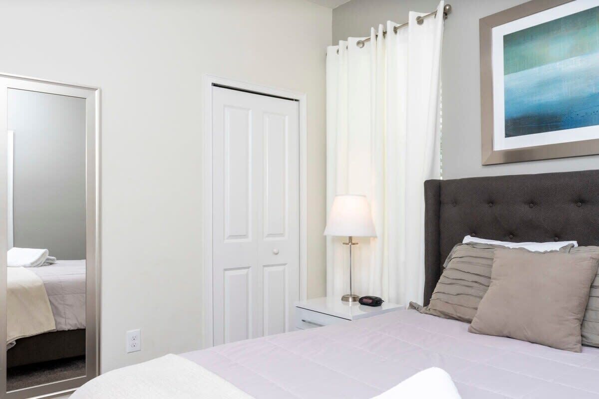 Habitación de hotel con cama, mesita de noche, lámpara, puerta y un cuadro en la pared.