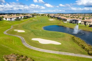 Ein Golfplatz mit Bunkern, einem Teich und Wohnhäusern im Hintergrund.