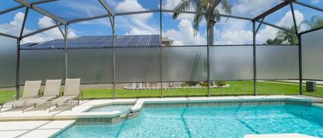 A swimming pool with a glass enclosure, lounge chairs, and a view of solar panels.
