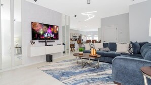 A modern living room with a flat-screen TV, a blue sofa, a coffee table, and a patterned rug. - Family-friendly House With Game Room & Private Pool (Davenport)