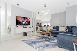 Ein modernes Wohnzimmer mit einem Flachbildfernseher, einem blauen Sofa, einem Couchtisch und einem gemusterten Teppich.