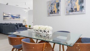 A modern living room with a glass-top dining table, wooden chairs, a grey sofa, and abstract paintings on the wall. - Family-friendly House With Game Room & Private Pool (Davenport)