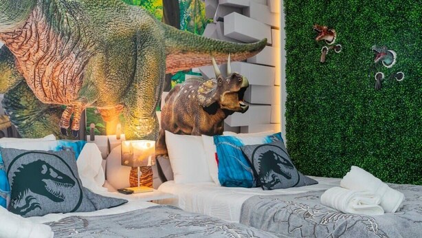 A bedroom with a dinosaur-themed bedspread, a green wall with dinosaur cutouts, and a small dinosaur figurine on the nightstand. - Family-friendly House With Game Room & Private Pool (Davenport)