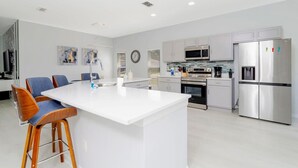 A modern kitchen with white cabinetry, a central island, stainless steel appliances, and a dining area with bar stools. - Family-friendly House With Game Room & Private Pool (Davenport)