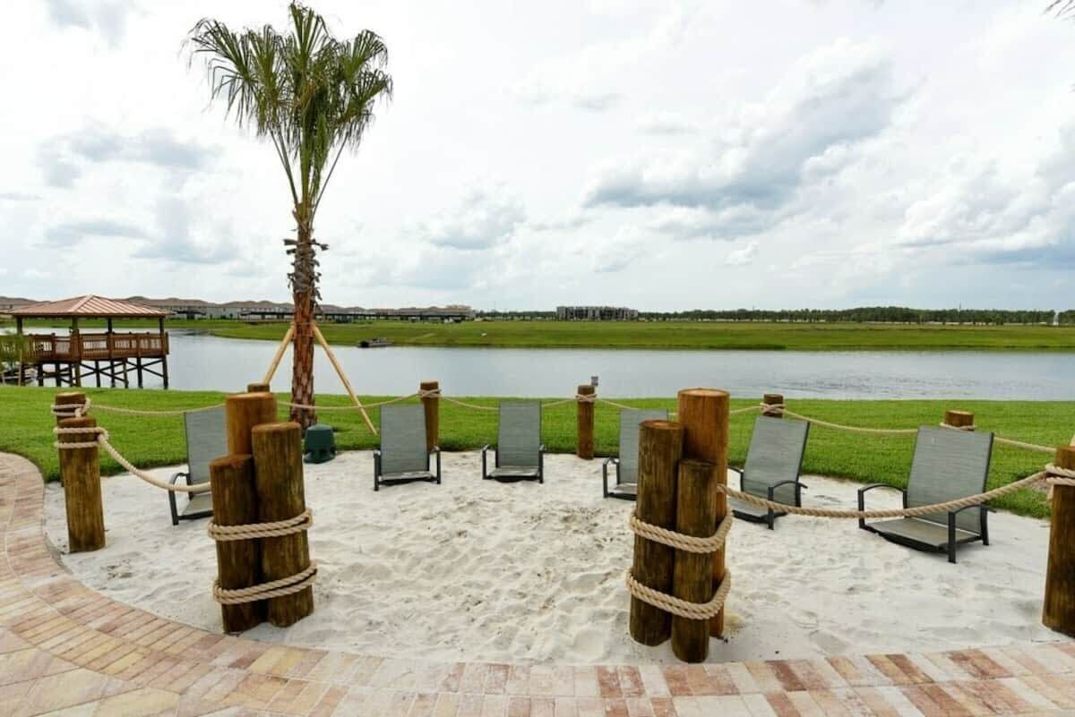 Zona de playa con sillas de descanso, una palmera y vista a un lago.