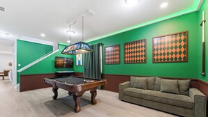 A pool table in a room with green walls, a sofa, and framed artwork. - Themed Disney Home w/ Pool & Game Room (Kissimmee)
