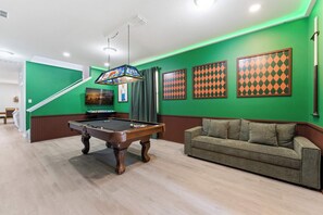 A pool table in a room with green walls, a sofa, and framed artwork. - Themed Disney Home w/ Pool & Game Room (Kissimmee)
