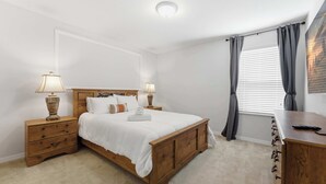 A bedroom with a wooden bed, bedside tables, lamps, a desk, and a window with curtains. - Themed Disney Home w/ Pool & Game Room (Kissimmee)