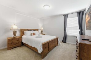 A bedroom with a wooden bed, bedside tables, lamps, a desk, and a window with curtains. - Themed Disney Home w/ Pool & Game Room (Kissimmee)