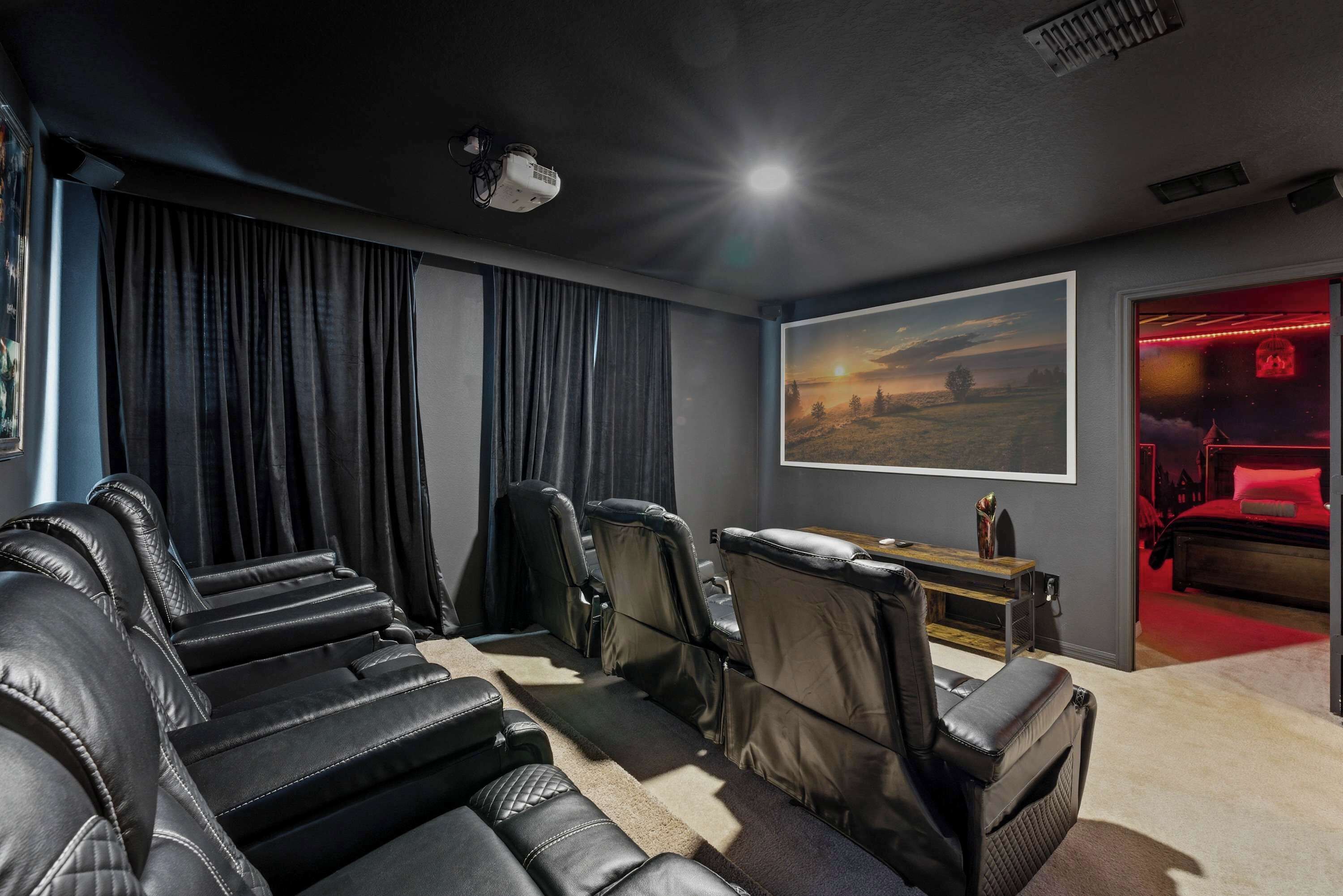 A home theater with leather reclining seats, a projector, and a large landscape painting.