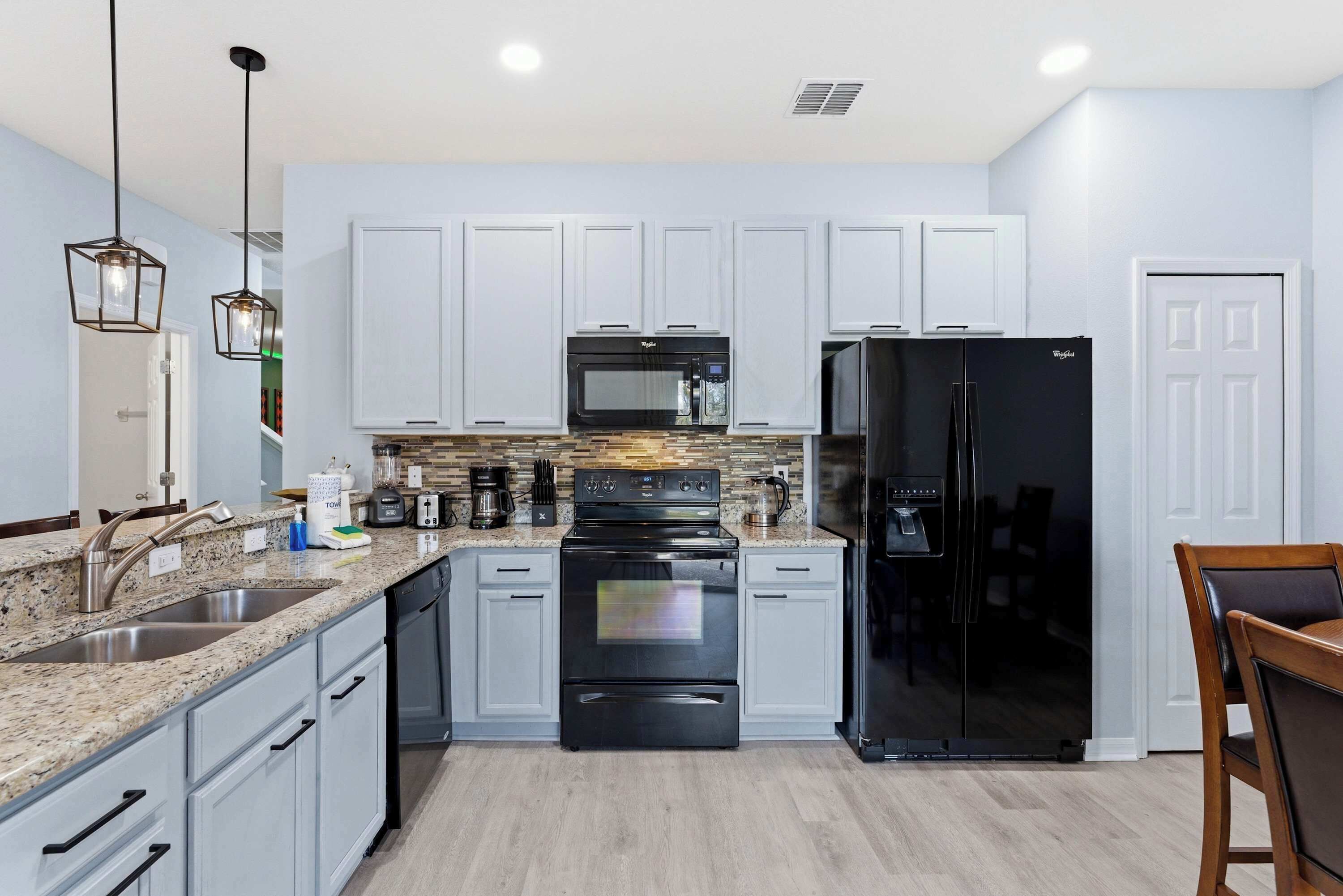 A modern kitchen with white cabinets, a black refrigerator, a microwave, and a stove.
