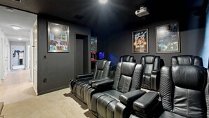 A home theater room with leather reclining seats, a projector, and movie posters on the wall. - Themed Disney Home w/ Pool & Game Room (Kissimmee)