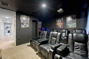 A home theater room with leather reclining seats, a projector, and movie posters on the wall. - Themed Disney Home w/ Pool & Game Room (Kissimmee)