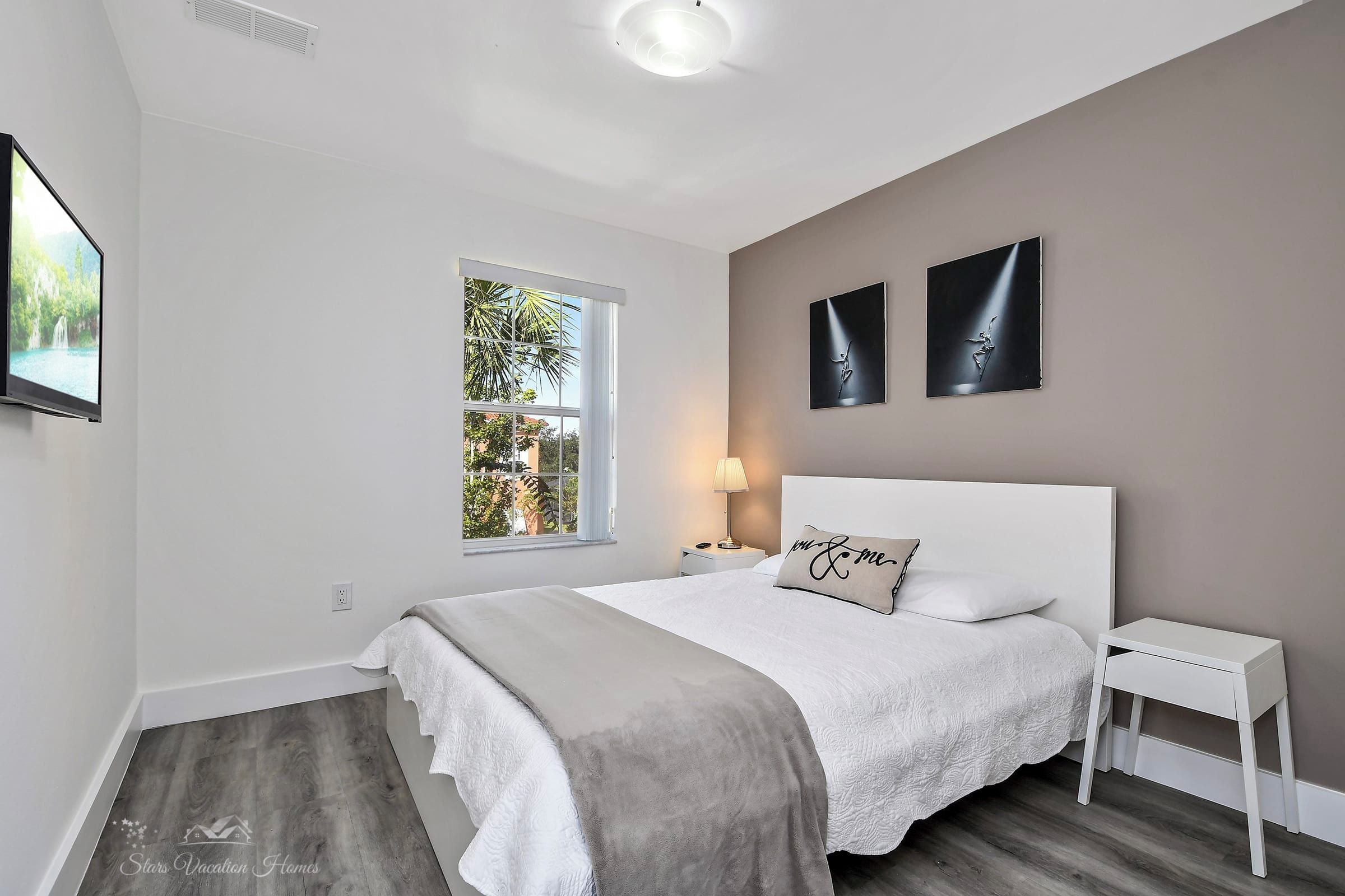 A bedroom with a bed, bedside table, window, and artwork on the wall.