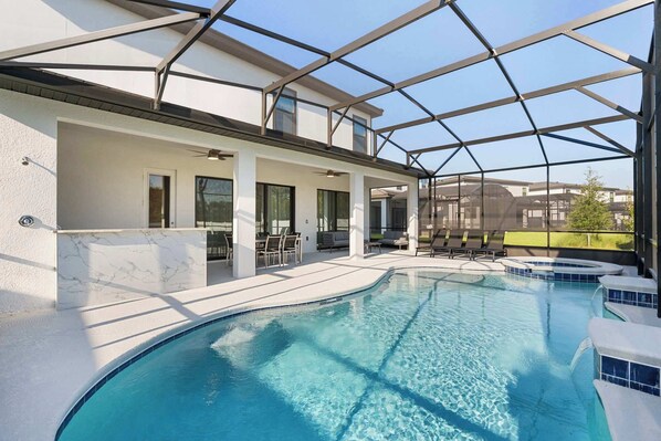A swimming pool with a glass enclosure, a covered patio area, and a view of neighboring buildings. - Themed 10bd Family Home w/ Private Pool & Game Room (Orlando)