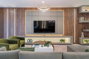 Ein modernes Wohnzimmer mit einem Flachbildfernseher an einer Holzwand, einem Sofa, einem Couchtisch und einem dekorativen Regal.