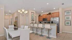 A modern kitchen with a central island, bar stools, and a dining area with a white table and chairs. - Family-friendly Paradise Palms Townhouse With Pool Access (Kissimmee)