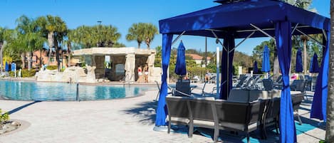 A poolside area with a covered seating area, lounge chairs, and umbrellas.