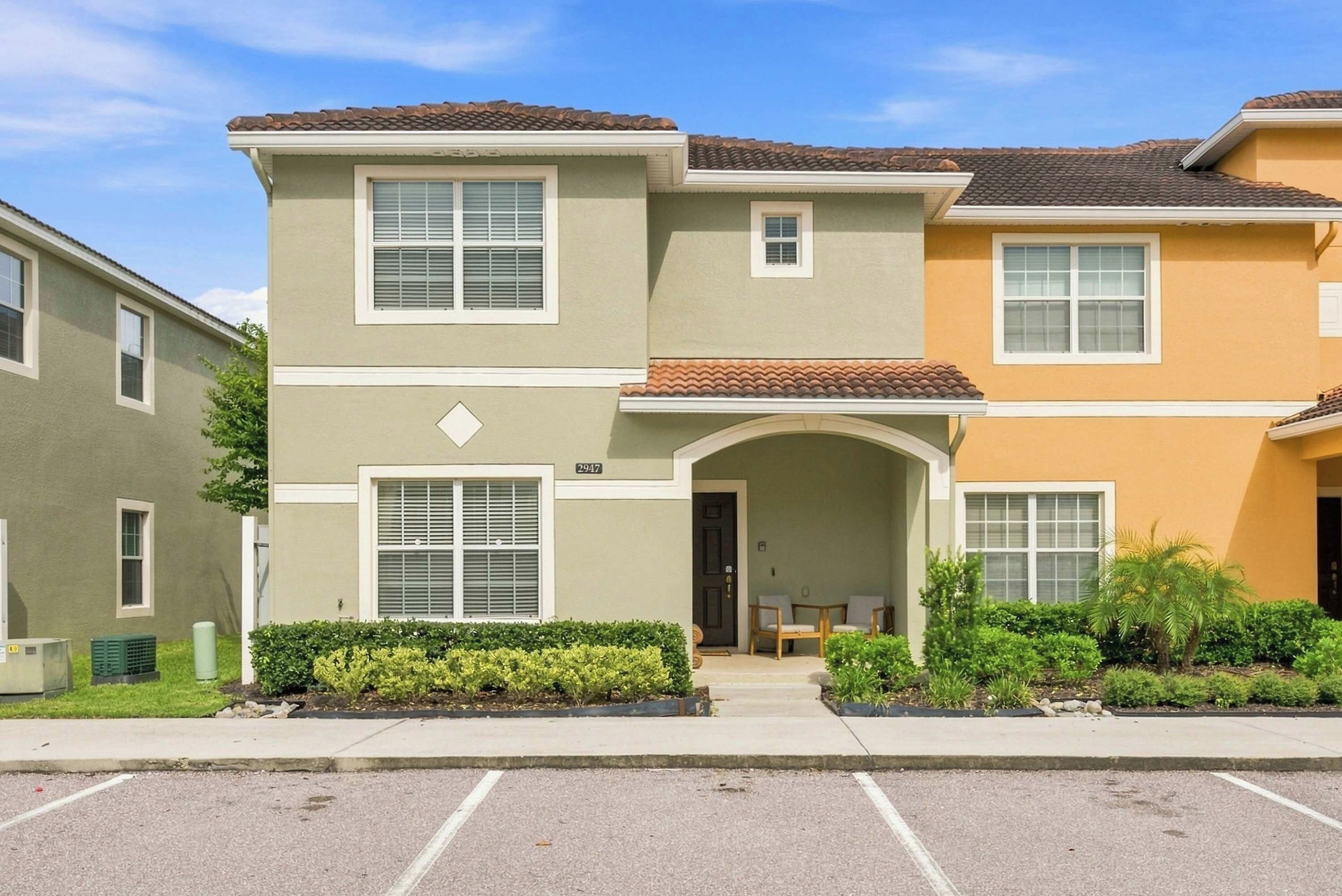 A two-story residential building with a flat roof, a front entrance with a small porch, and a parking lot in front.