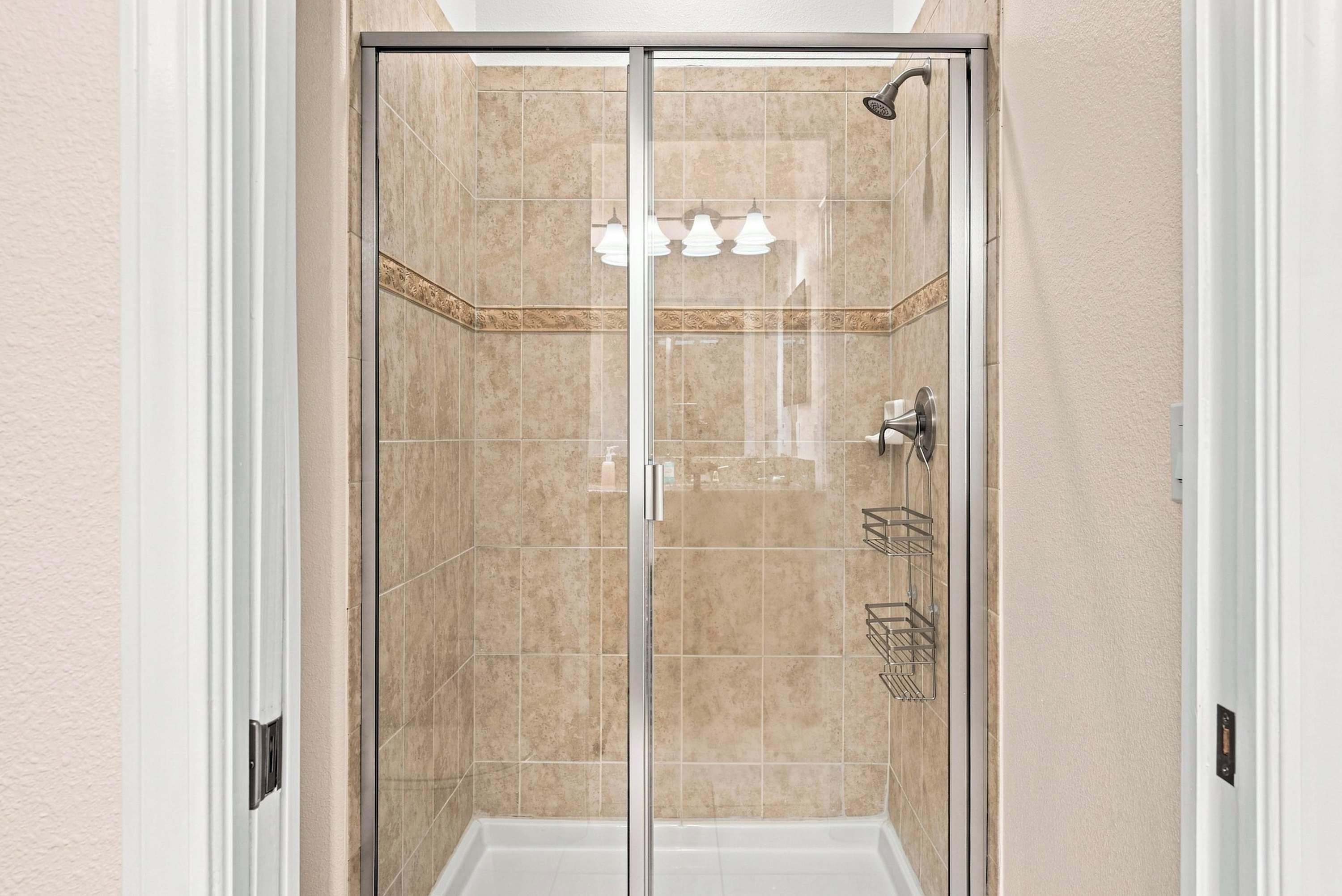 A walk-in shower with a glass door, beige tiles, a showerhead, and a towel rack.