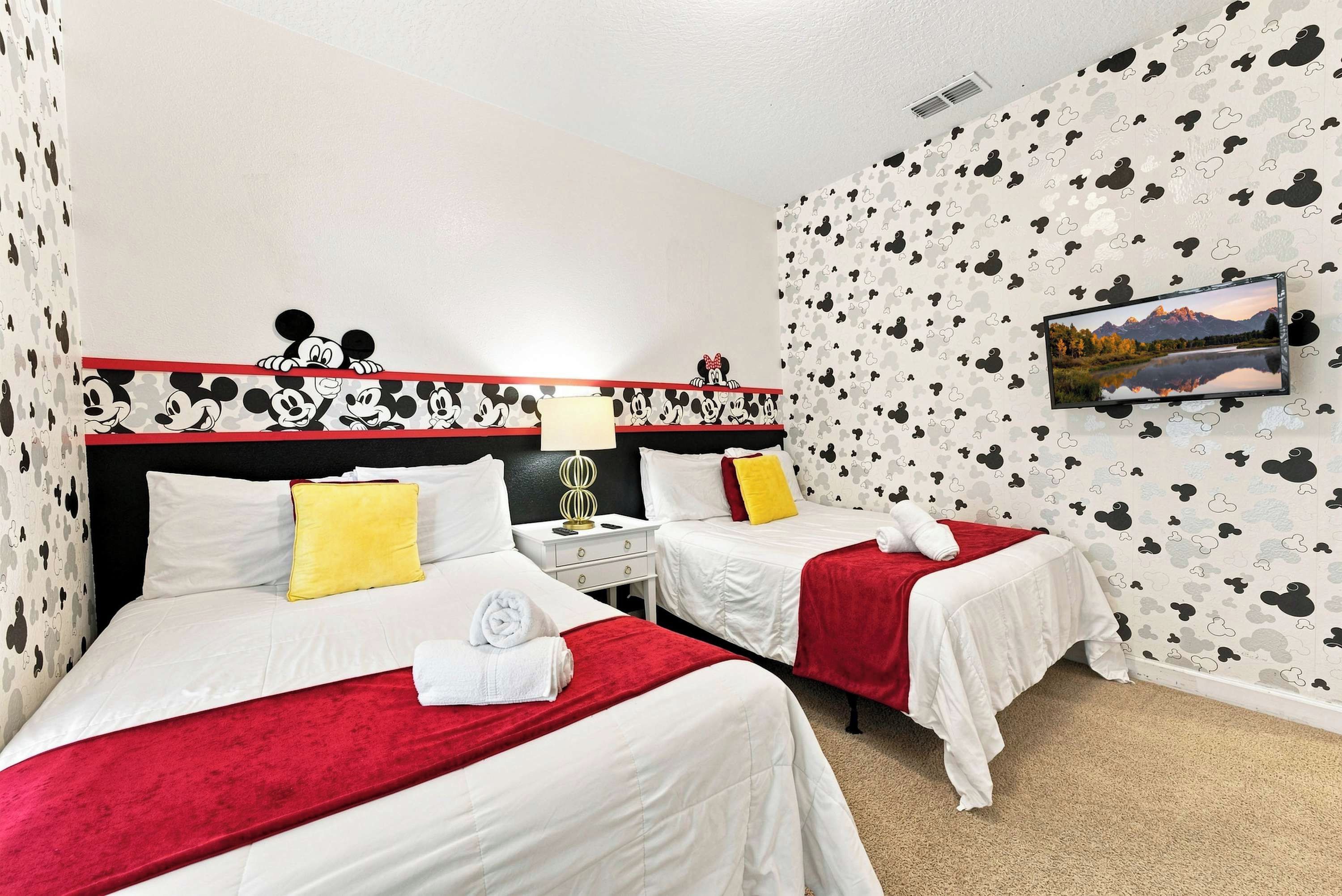 A hotel room with two beds, a television on the wall, and Mickey Mouse-themed wallpaper.