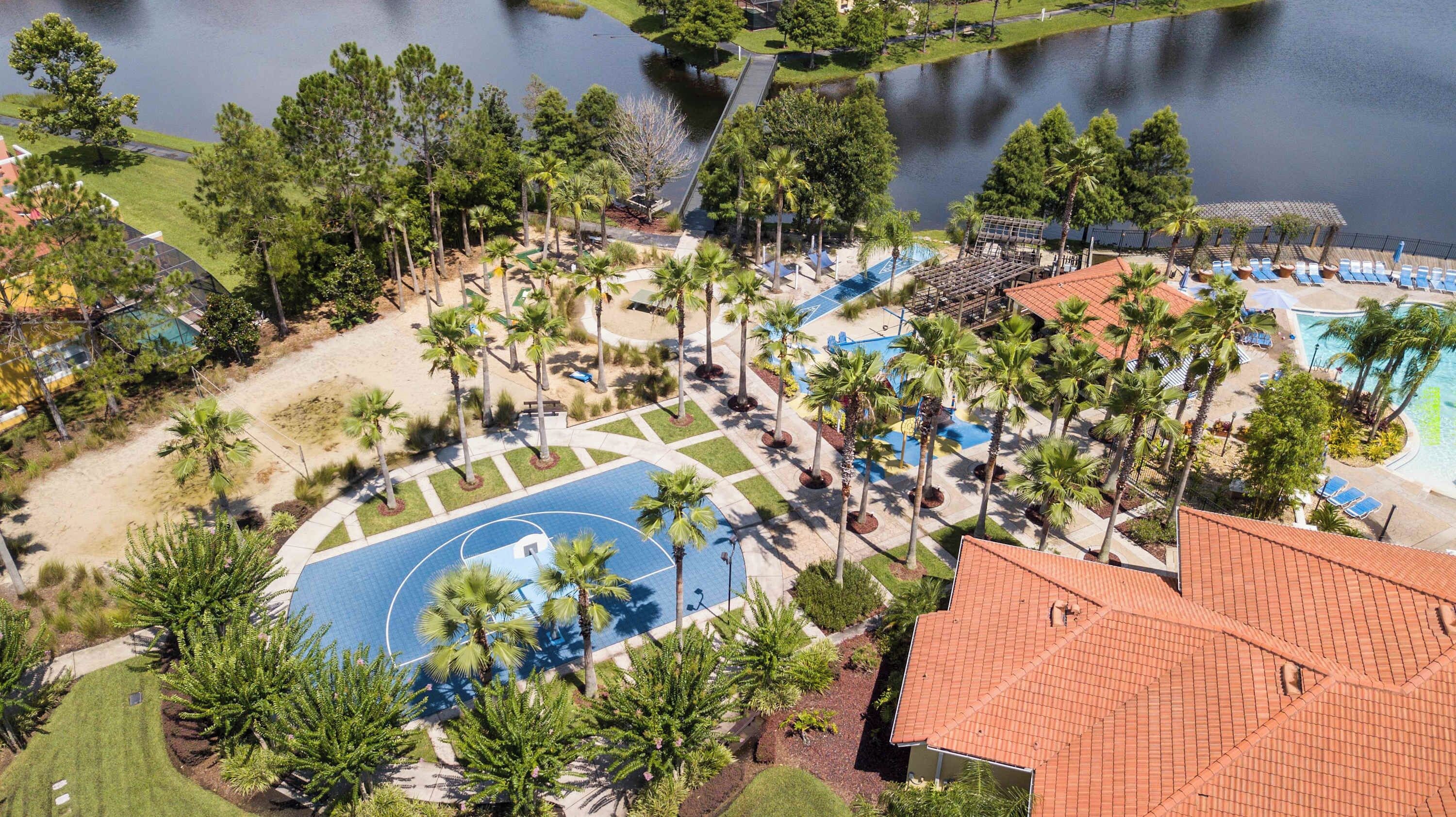 Un complexe hôtelier doté d’un terrain de basketball, de palmiers, d’une piscine et offrant une vue sur un lac.