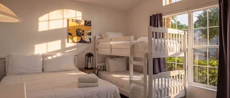 A bedroom with bunk beds, a large window with curtains, a wall-mounted lamp, and a painting.
