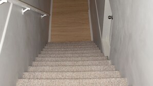 A staircase with a handrail, wooden floor, and a white wall.