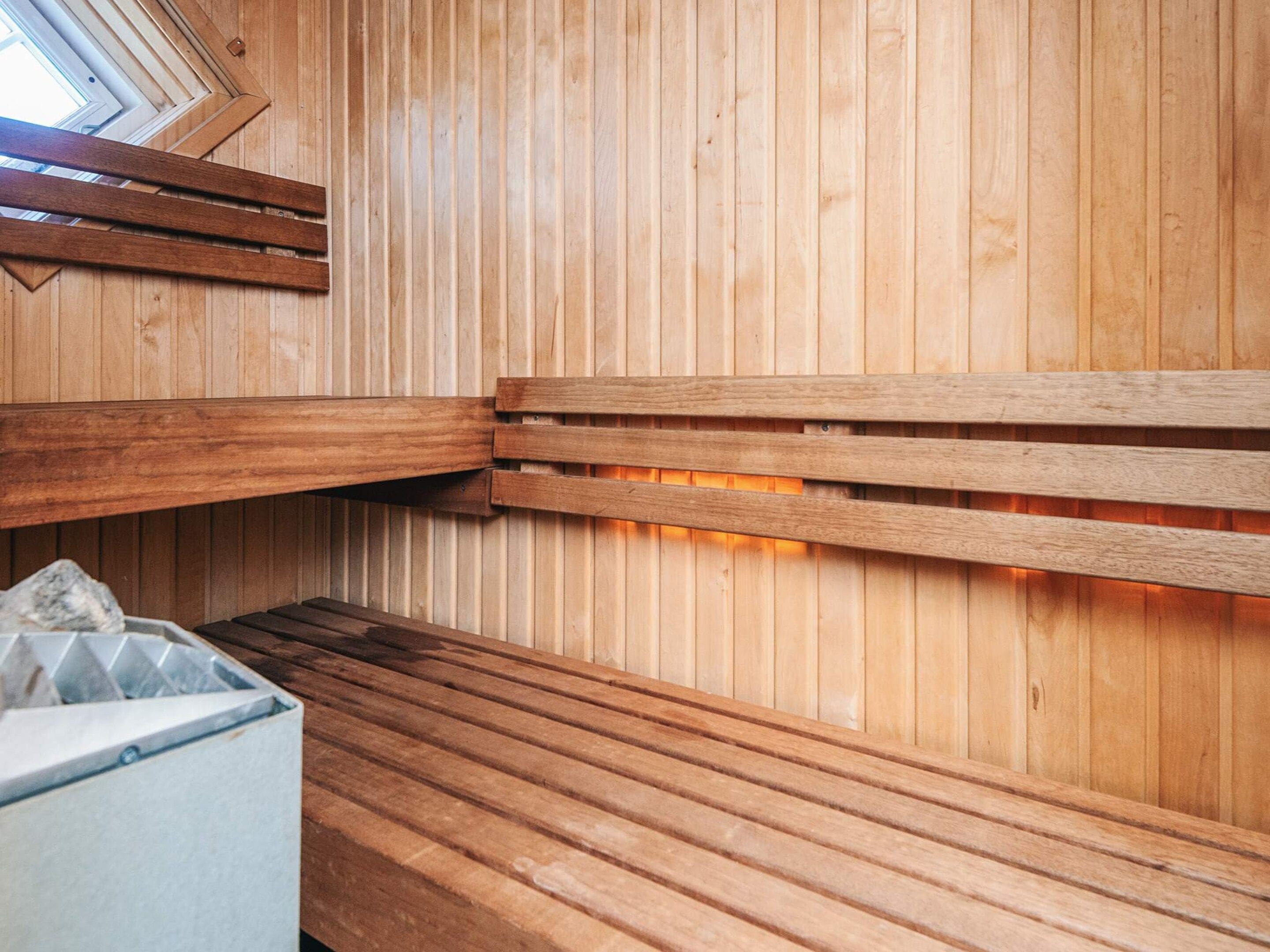 A sauna room with wooden benches and a stone container.