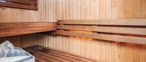 A sauna room with wooden benches and a stone container.