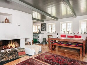 A spacious living room with a fireplace, wooden flooring, a dining area with red cushions, and a large window with multiple panes. - 5 Star Holiday Home in Fano (Fano)