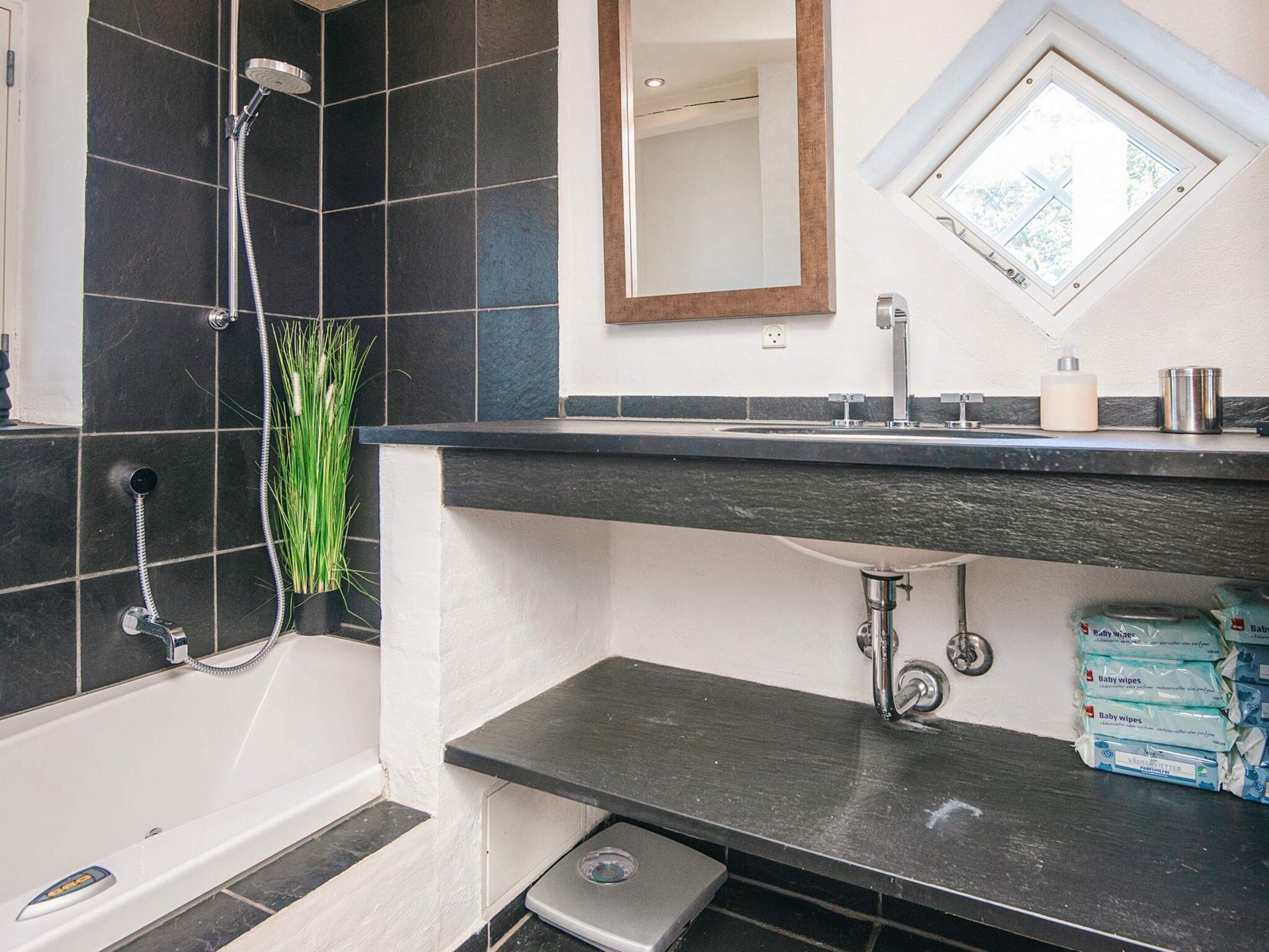 A bathroom with a shower, a sink, a mirror, and a window.