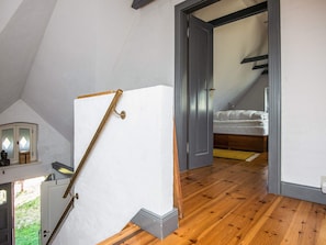 A room with a sloped ceiling, a bed with white bedding, and a wooden floor.
