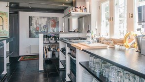 Een moderne keuken met een centraal eiland, een schilderij aan de muur en uitzicht op het buitengebied door grote ramen.