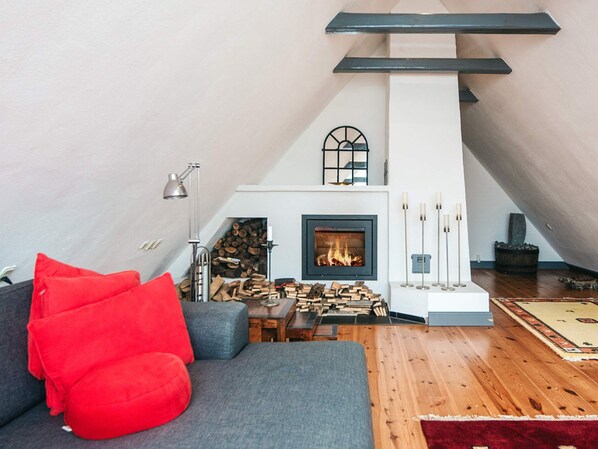 A cozy living room with a fireplace, a sofa with red cushions, and a wooden floor.