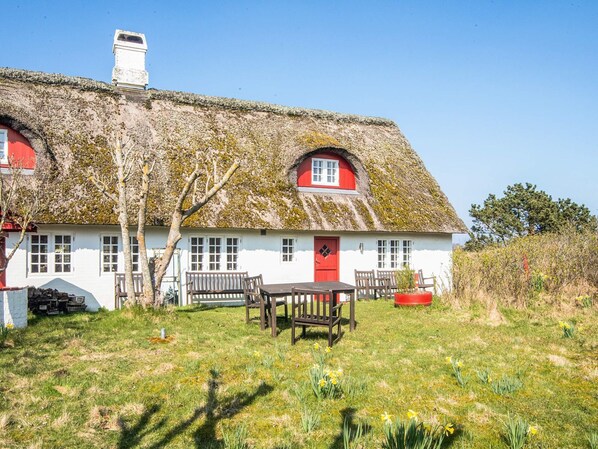 A traditional house with a thatched roof, a red door, and a small garden with daffodils. - 5 Star Holiday Home in Fano (Fano)